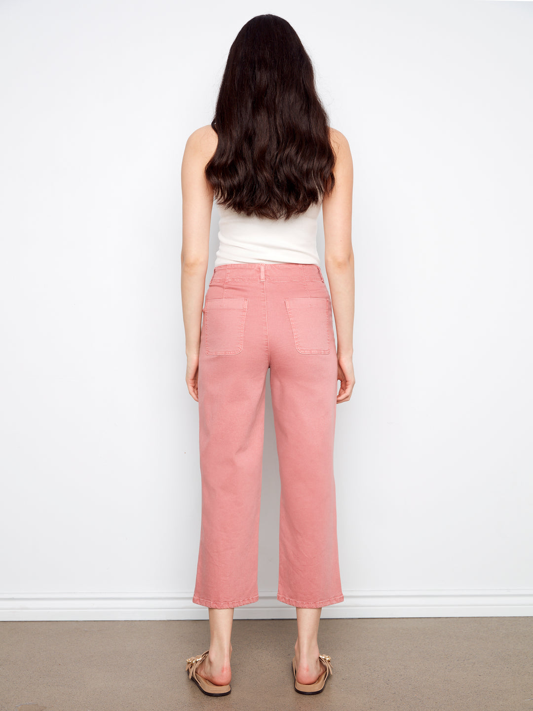 Person wearing a white top and pink pants against a white wall