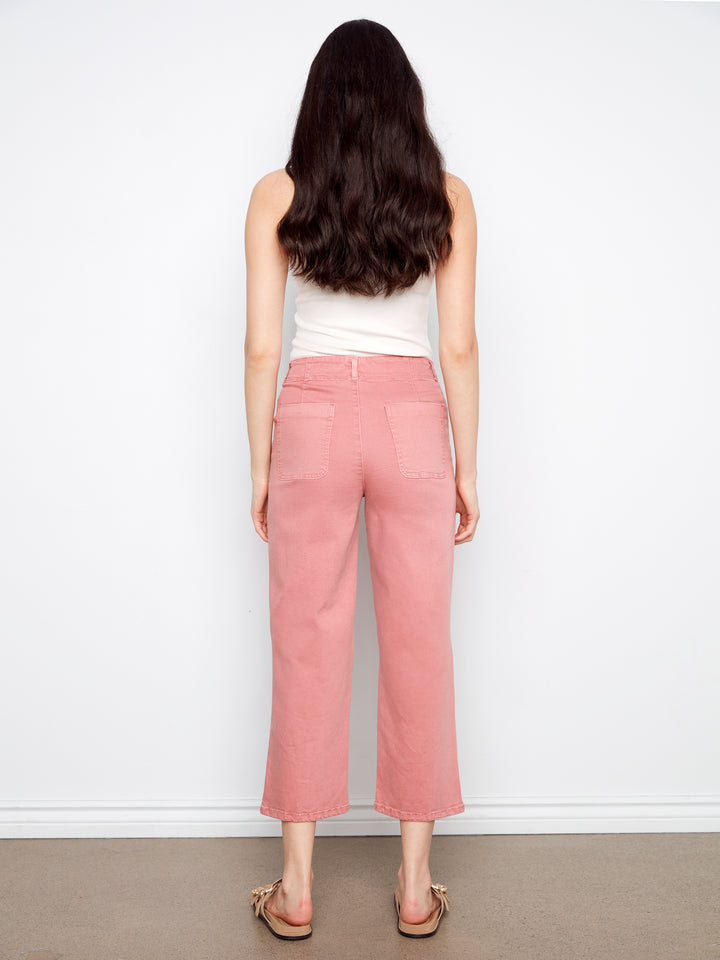 Person wearing a white top and pink pants against a white wall