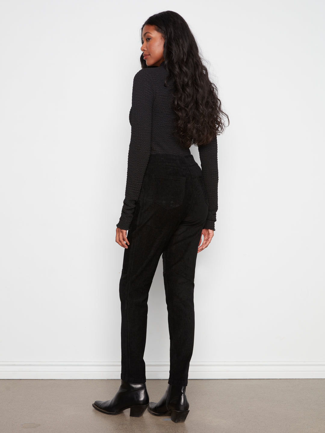 Person wearing a black outfit standing against a white wall