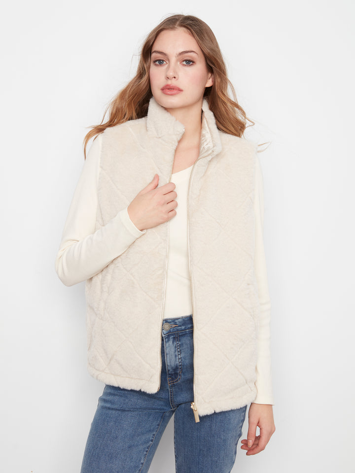 A woman modeling a cream-colored quilted zip-up vest over a matching cream long-sleeve top and blue jeans, set against a plain white studio background.