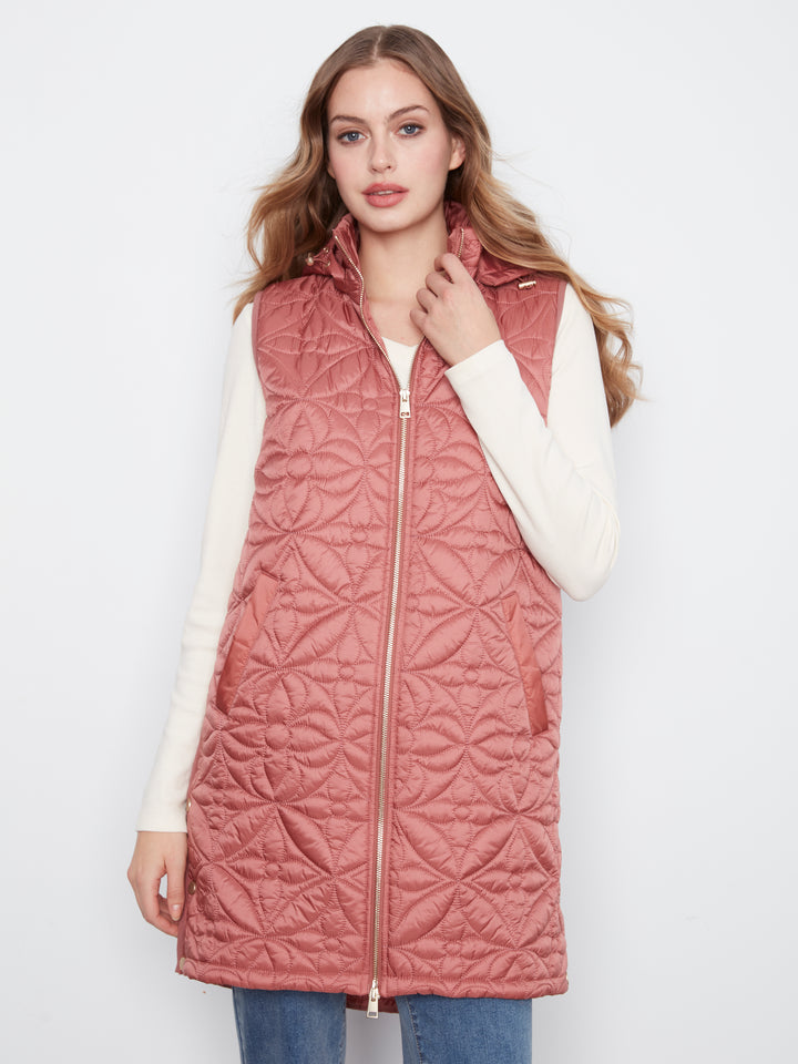 A woman wearing a dusty rose quilted sleeveless puffer vest over a white long-sleeve top and blue jeans, standing against a plain white studio background.