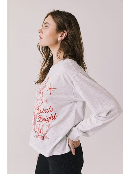 Woman wearing a light gray sweatshirt with red text and graphics on a plain background