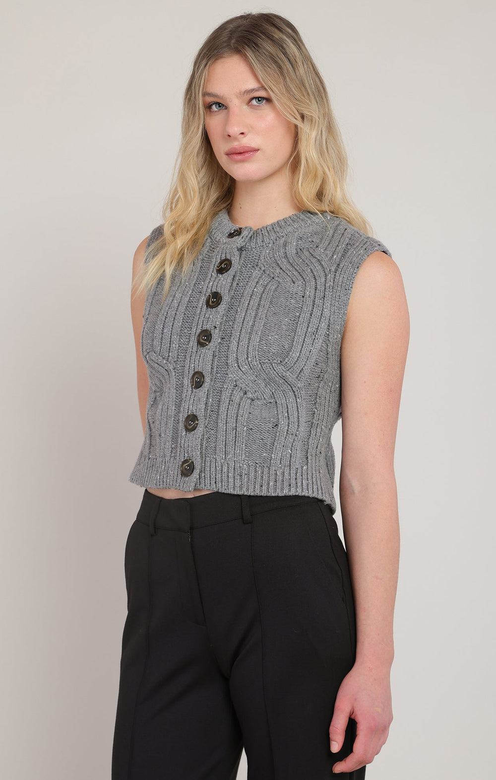 Woman wearing a gray knitted vest with black buttons on a plain background