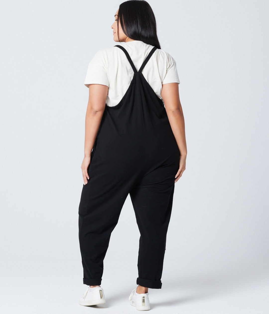 Person wearing a black overalls with a white shirt underneath on a plain background