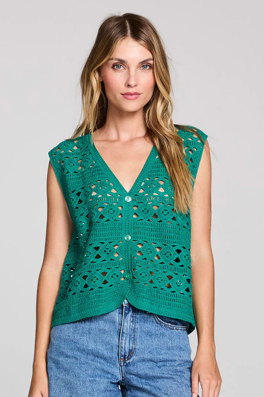 Woman wearing a green crochet vest and denim shorts on a gray background