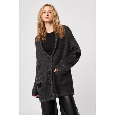 Woman wearing a dark gray cardigan over a black top on a light gray background