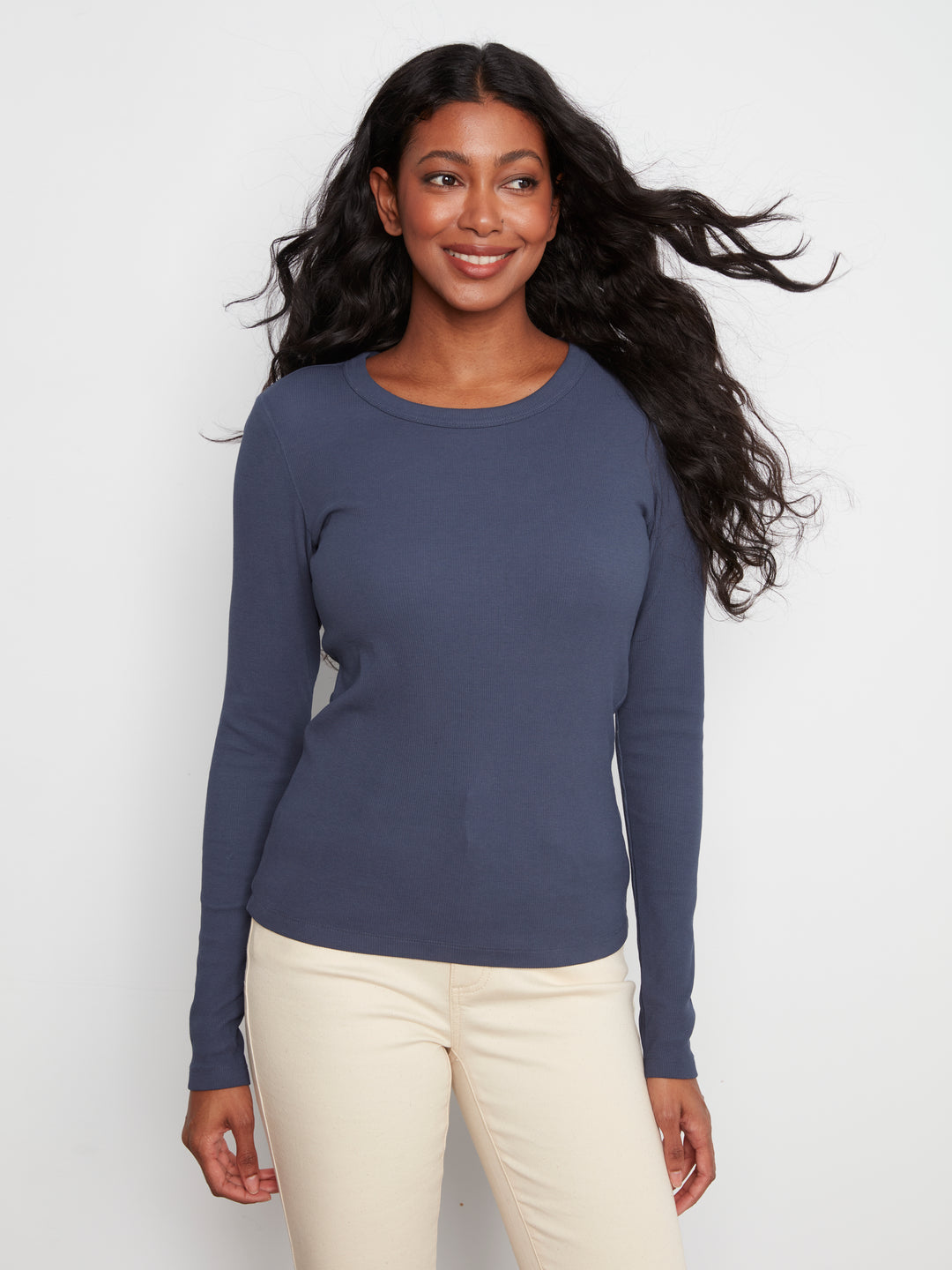 Woman wearing a blue long-sleeve top and white pants against a white background