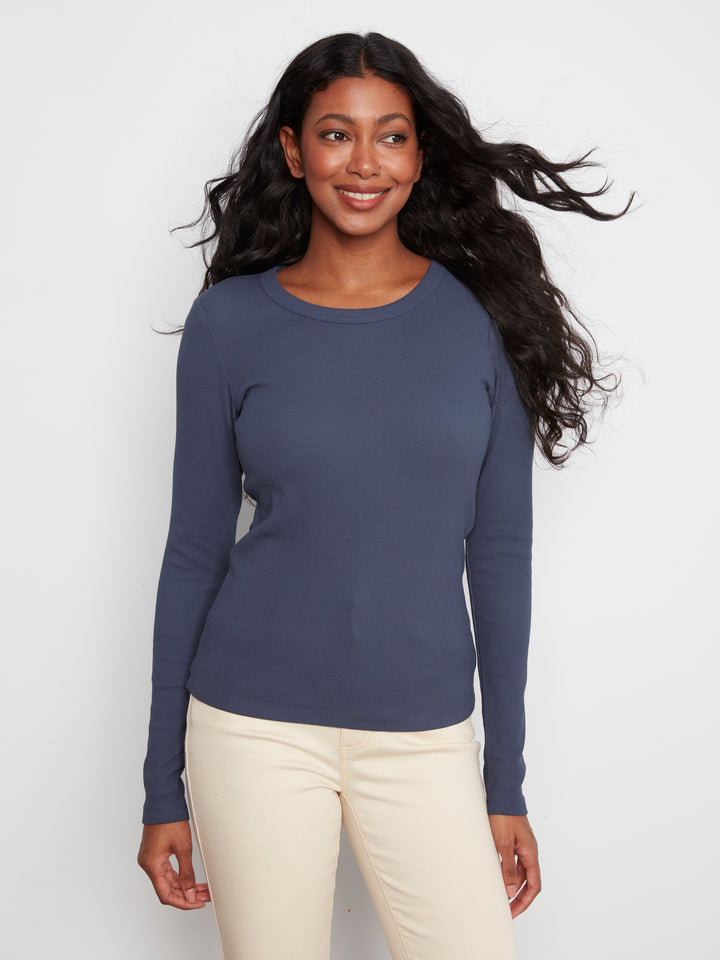 Woman wearing a blue long-sleeve top and white pants against a white background