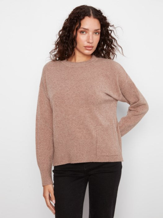 A woman modeling a dusty rose knit sweater with black pants against a plain light gray background.
