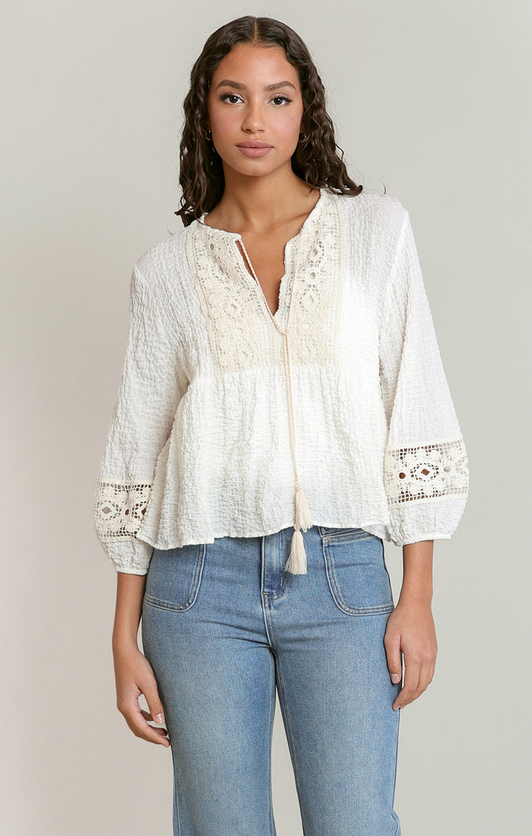 Woman wearing a white lace blouse and blue jeans against a plain background
