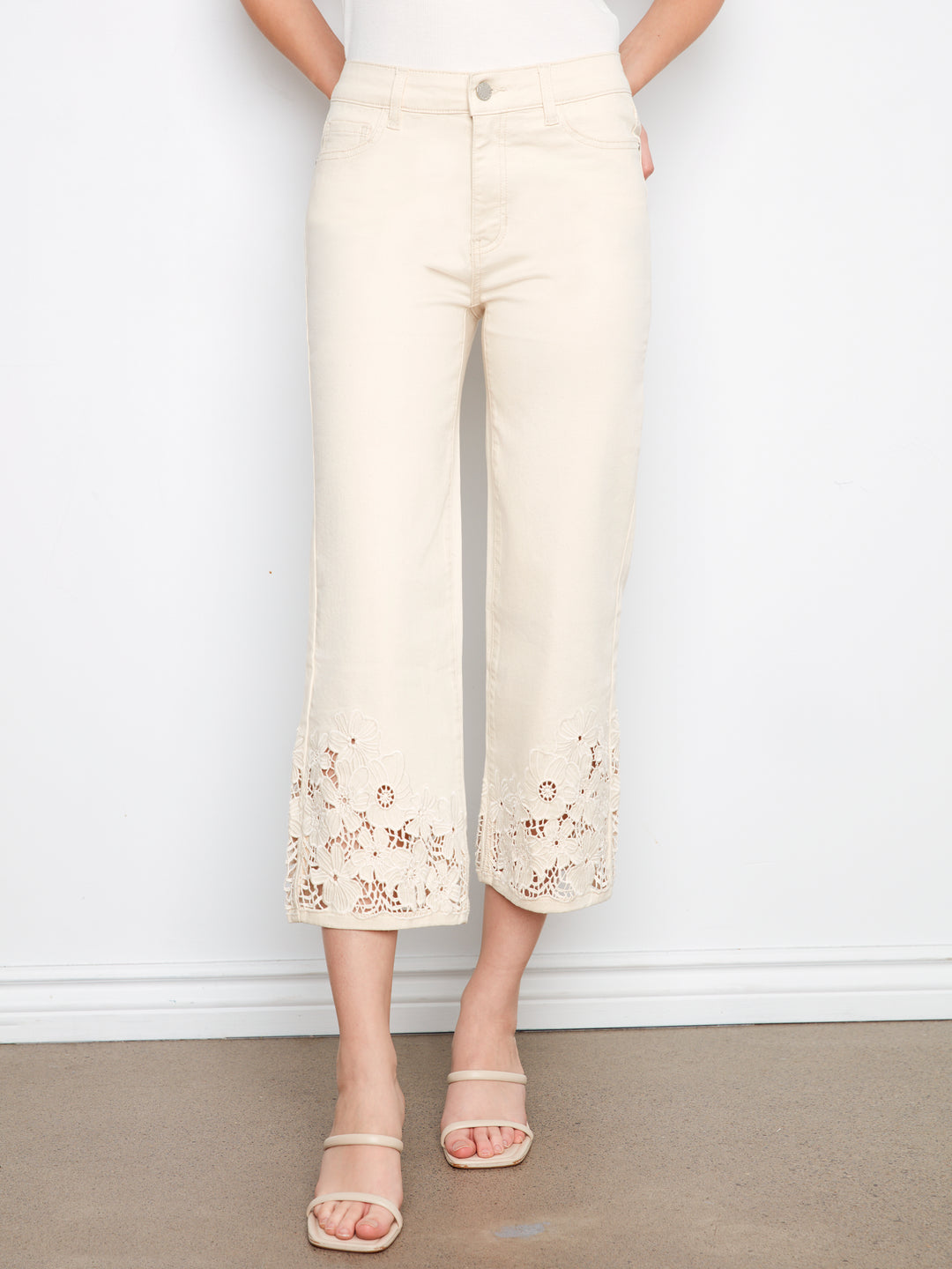 Person wearing cream-colored pants with floral embroidery on a plain background