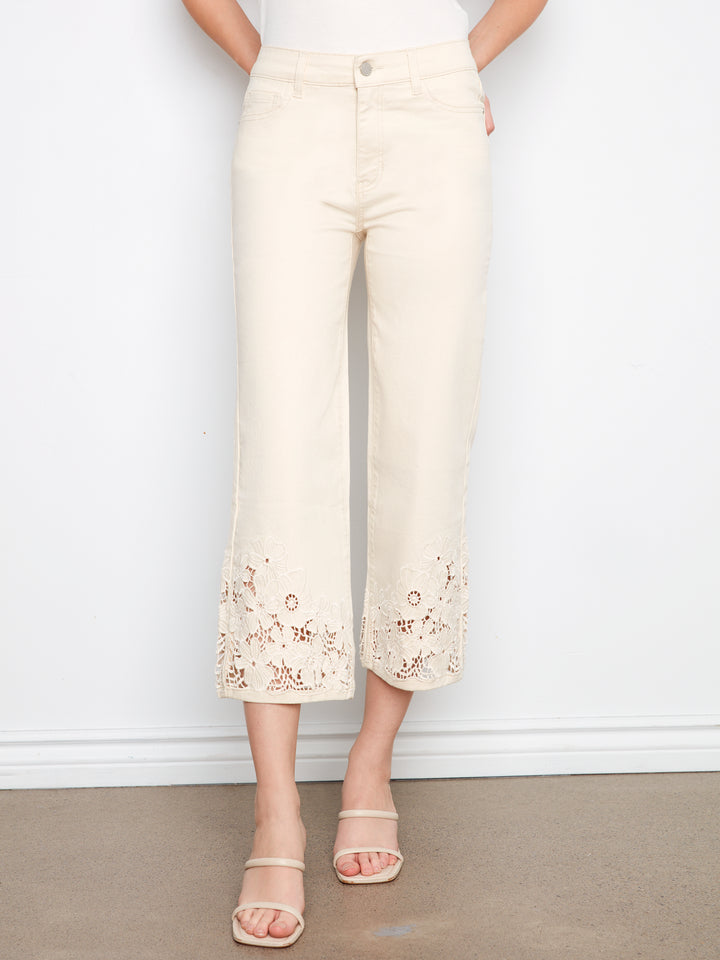 Person wearing cream-colored pants with floral embroidery on a plain background