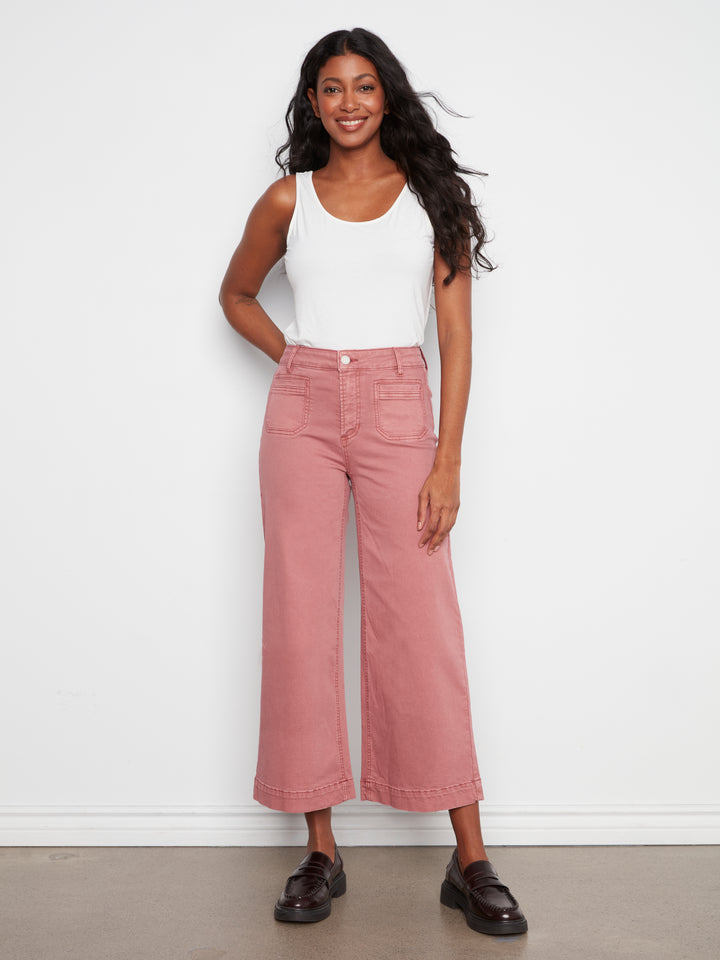 Woman wearing a white tank top and pink pants against a white background