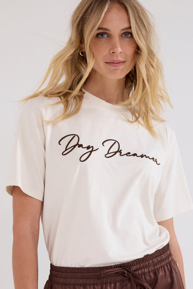 A woman wearing a cream-colored short-sleeve t-shirt with &