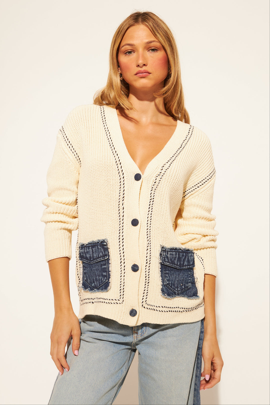 Woman wearing a cream cardigan with blue pocket details on a white background