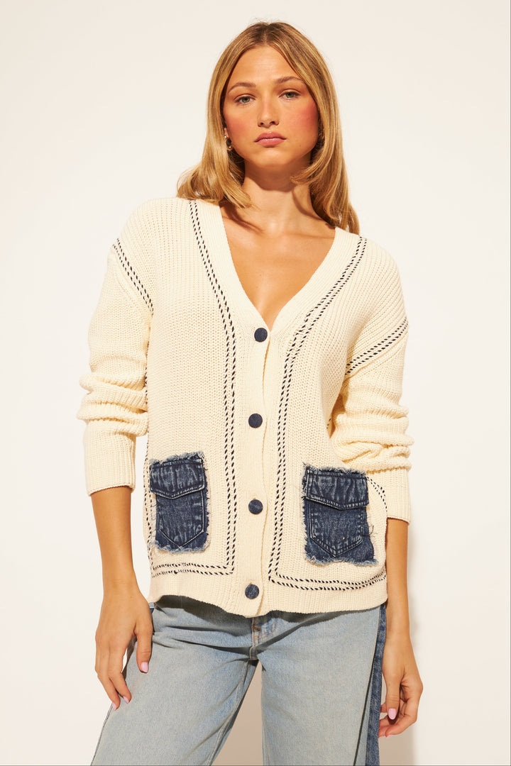 Woman wearing a cream cardigan with blue pocket details on a white background