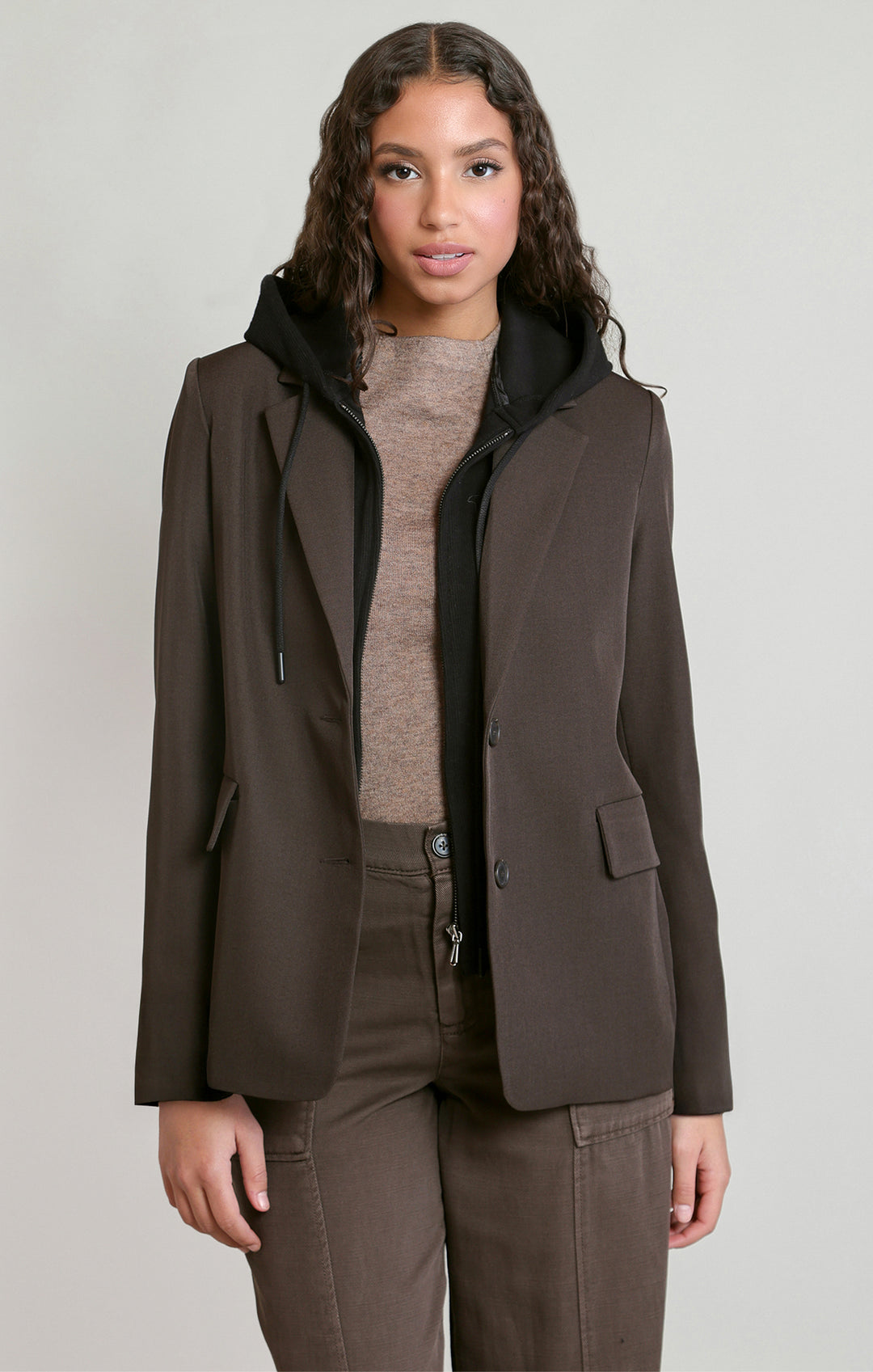 Woman wearing a brown coat with a hood on a plain background