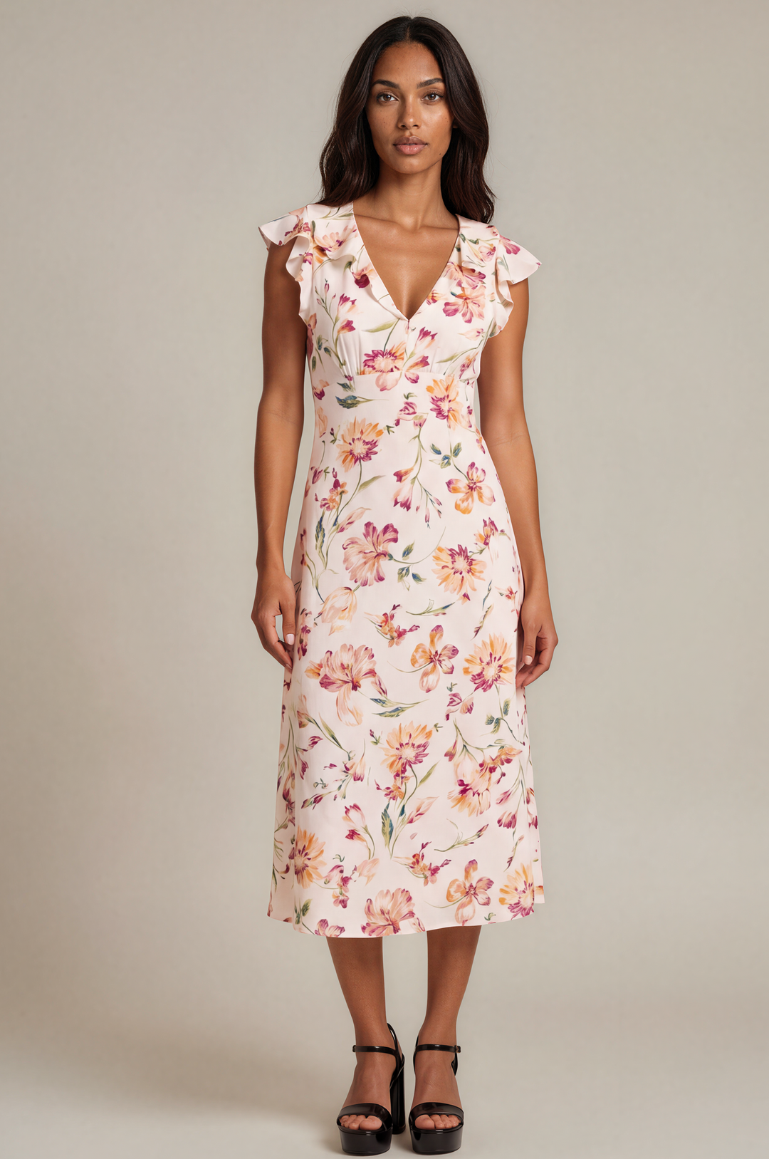 A woman modeling a sleeveless midi dress with a floral print, ruffled cap sleeves, and a V-neckline, paired with black platform sandals against a neutral studio background.