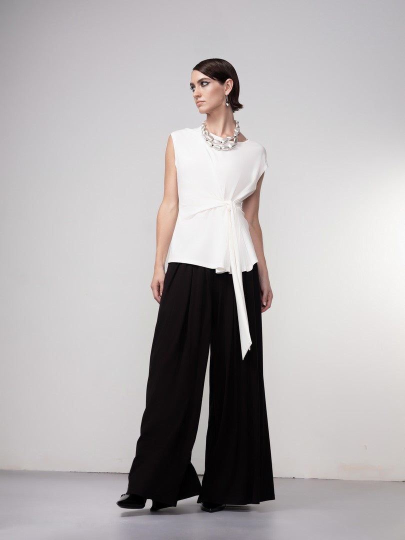 Woman wearing a white sleeveless top and black wide-leg pants on a plain background