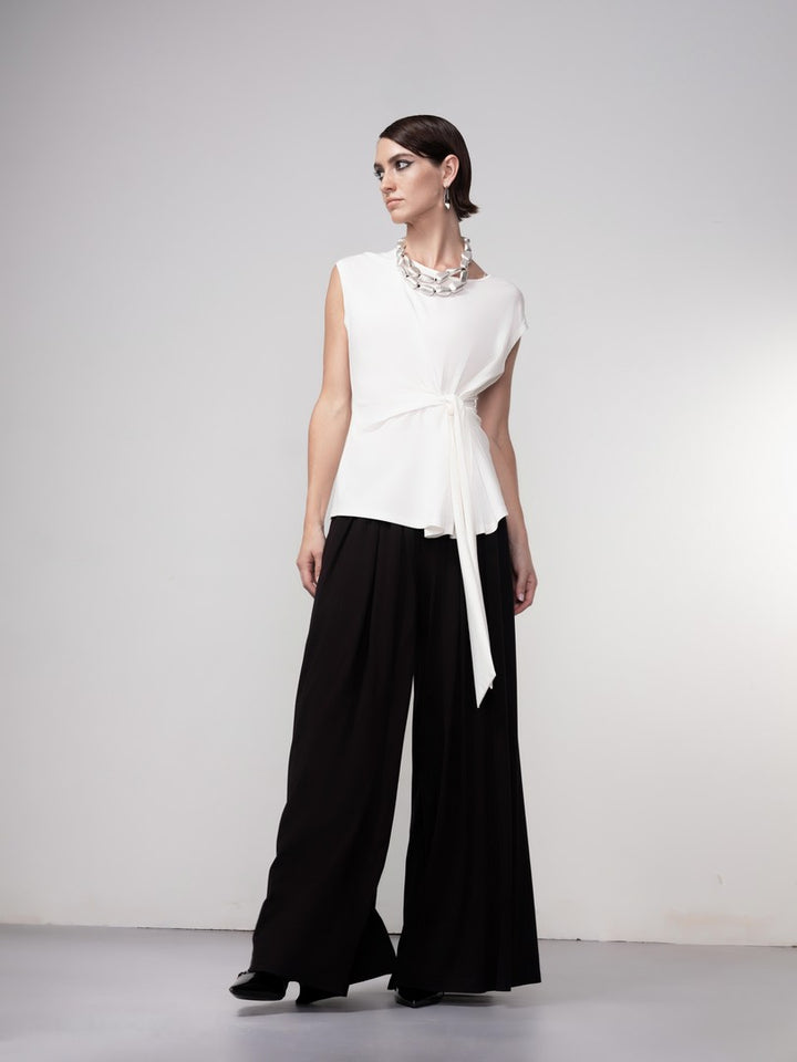Woman wearing a white sleeveless top and black wide-leg pants on a plain background