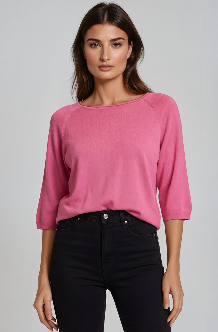 Woman wearing a pink blouse and black pants against a gray background
