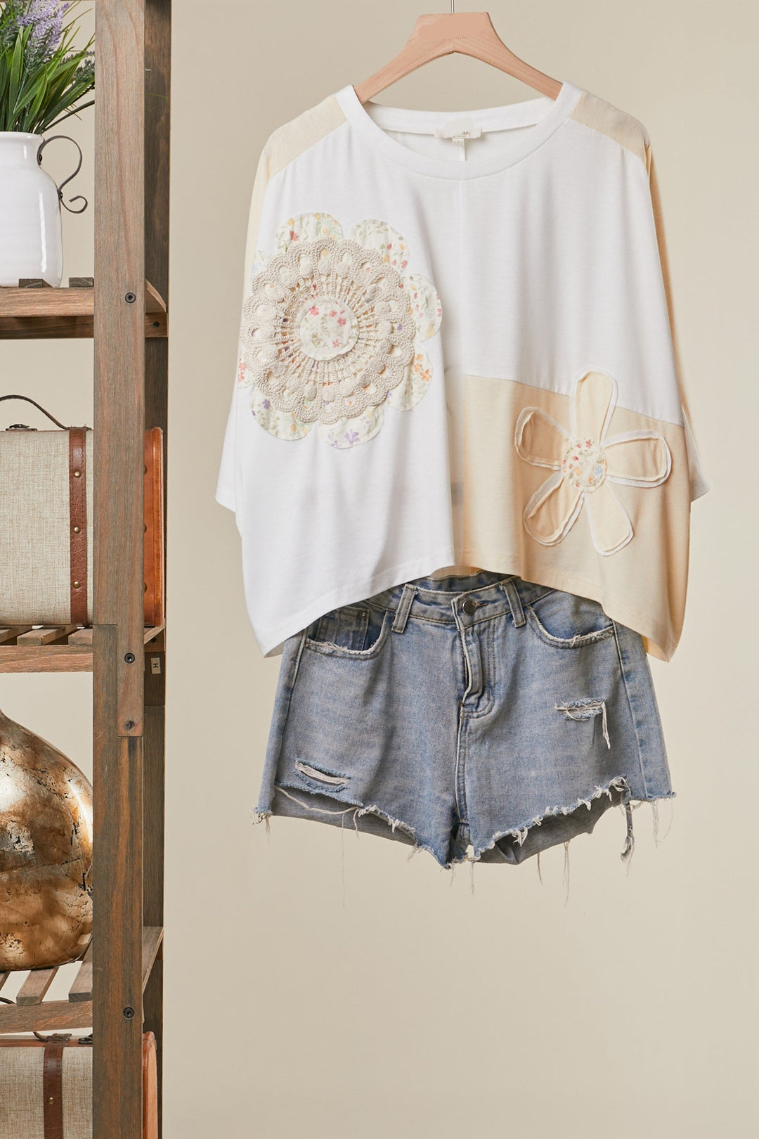 White top with floral embroidery and denim shorts on a hanger against a neutral wall.