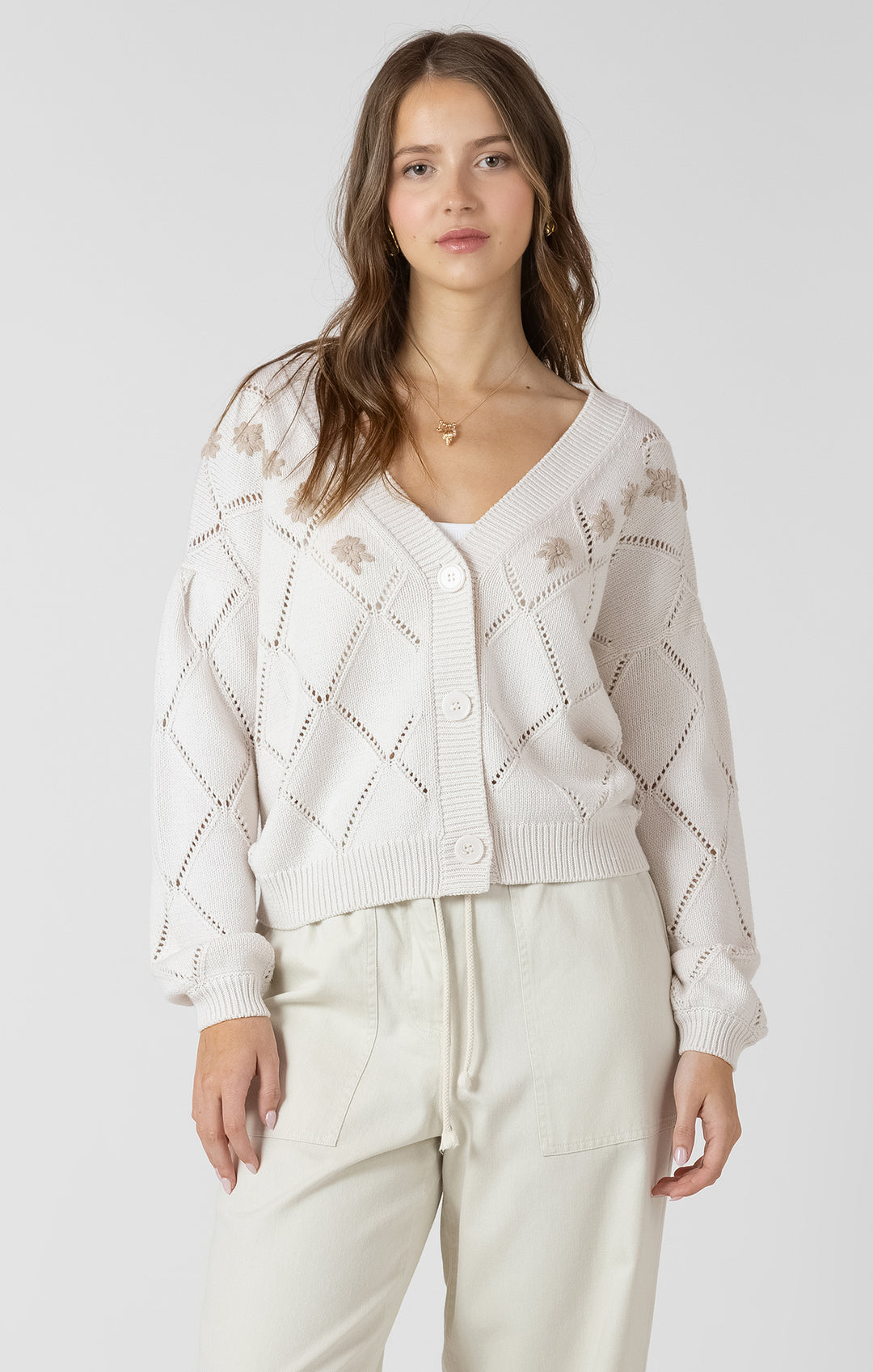 Woman wearing a white knit cardigan and pants on a plain background