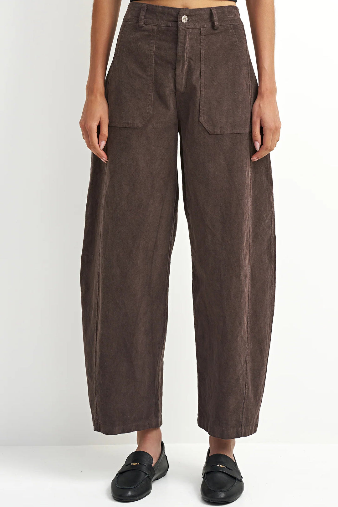 A model is shown from the waist down wearing dark brown wide-leg cropped trousers with a textured corduroy-like finish, paired with black leather loafers, against a plain white studio background.