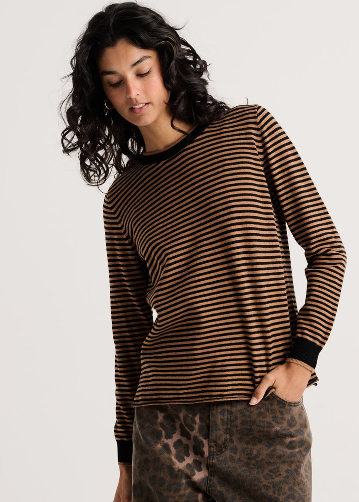 A woman wearing a brown and black horizontally striped long-sleeve top with black trim, paired with brown leopard-print pants, against a light gray studio background.