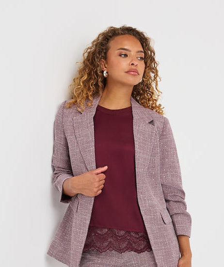 A woman modeling a matching two-piece blazer and trouser set in a dusty mauve-purple color with a subtle houndstooth pattern, styled with a burgundy top and burgundy loafers against a plain white studio background.