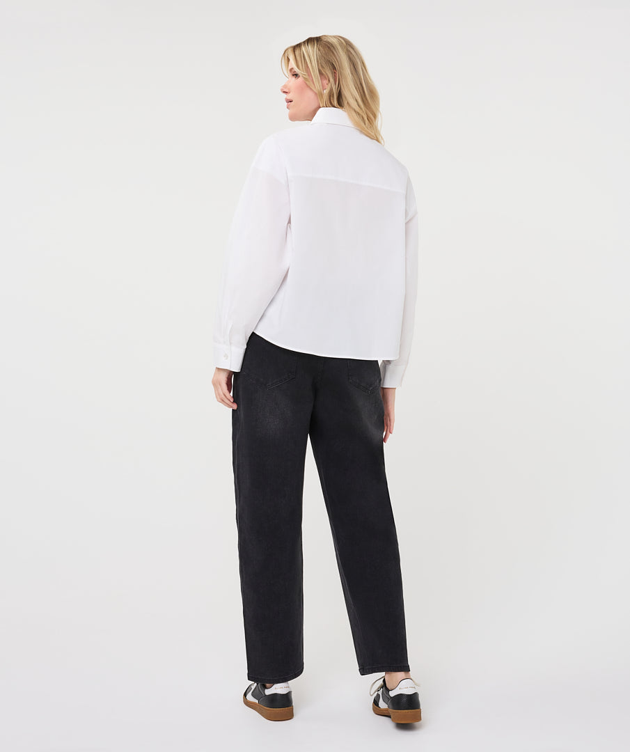 A woman is shown from behind wearing a white long-sleeve blouse and black wide-leg trousers, standing against a plain light gray studio background.