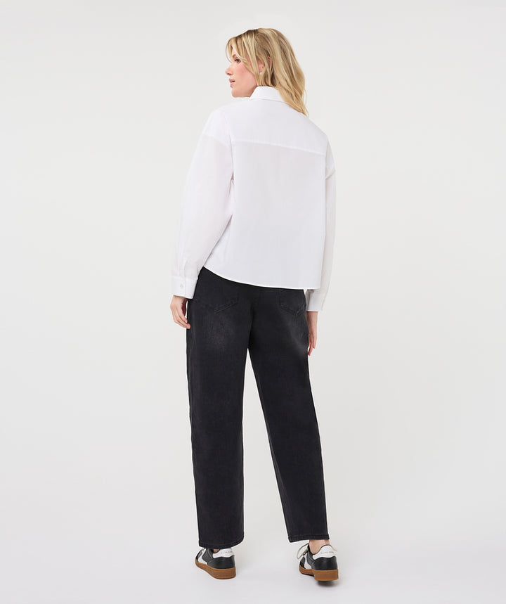 A woman is shown from behind wearing a white long-sleeve blouse and black wide-leg trousers, standing against a plain light gray studio background.