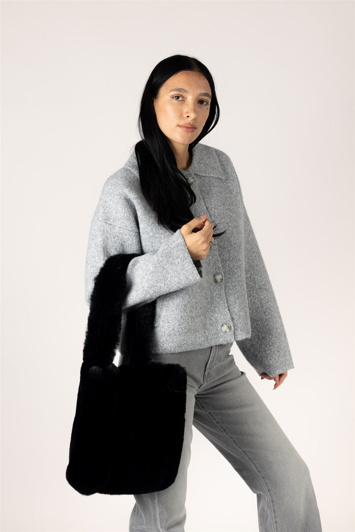 A woman modeling a light gray textured jacket and gray jeans, carrying a large black fuzzy shoulder bag against a plain light background.