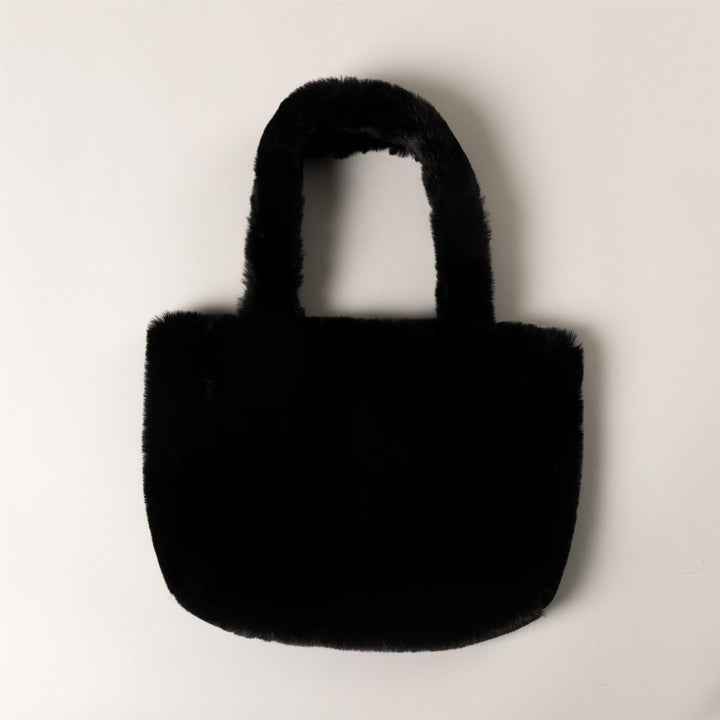 A small black faux fur tote bag with a rounded bottom and two short handles, photographed against a plain off-white background.