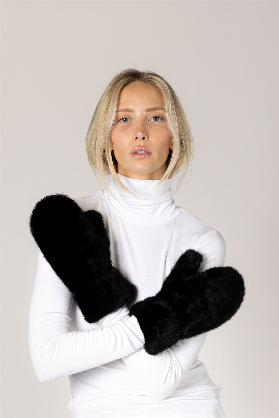 Woman wearing black gloves and a white turtleneck against a plain background