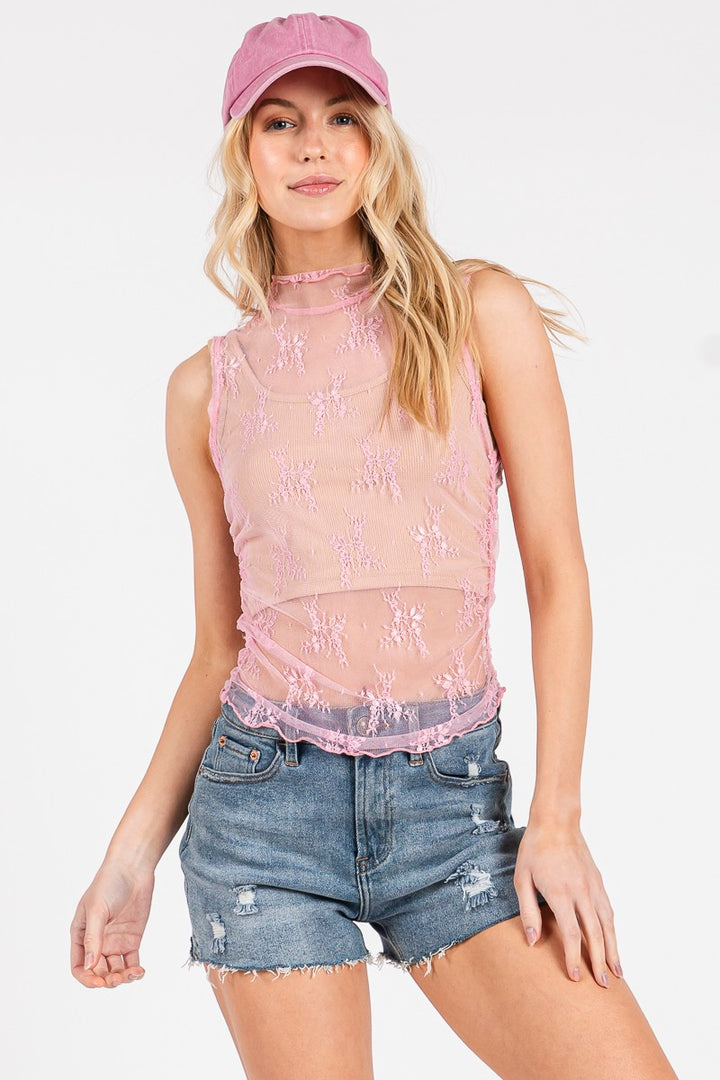 Woman wearing a pink mesh top and denim shorts with a pink cap on a white background