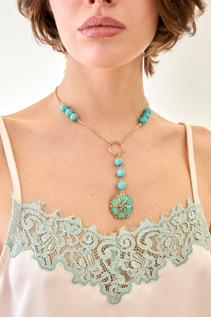 Woman wearing a turquoise necklace with a gold chain and pendant, against a neutral background.