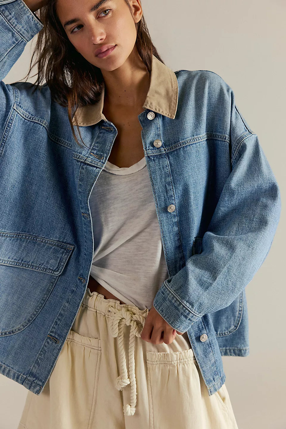 Woman wearing a blue denim jacket over a white shirt and beige pants on a neutral background