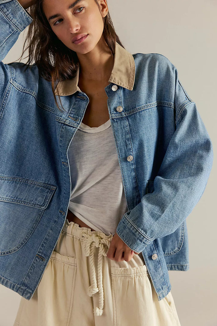 Woman wearing a blue denim jacket over a white shirt and beige pants on a neutral background