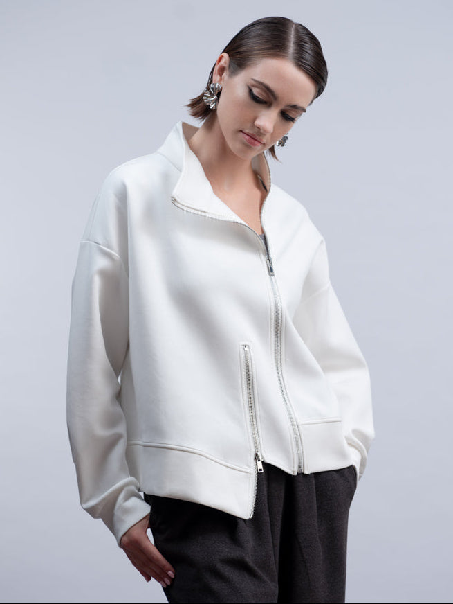 A woman wearing a white cropped zip-up jacket with a stand collar and black trousers, photographed against a light gray studio background.
