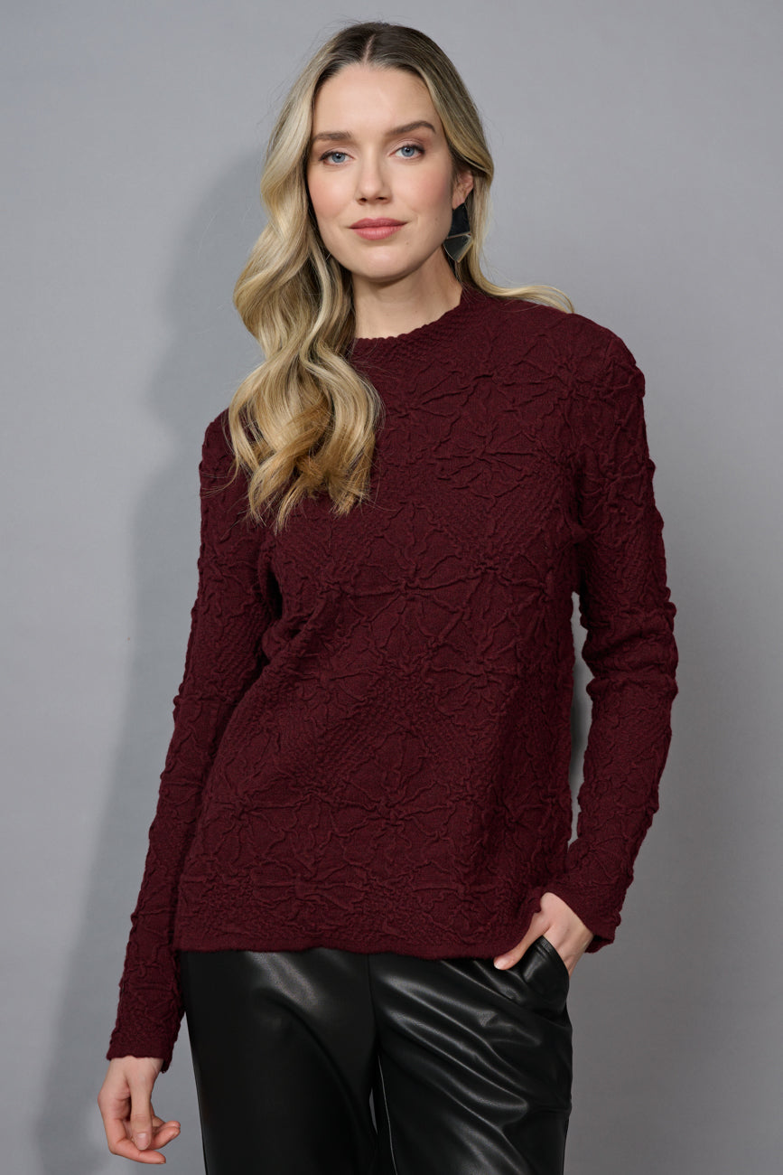 Woman wearing a burgundy cable knit sweater against a gray background