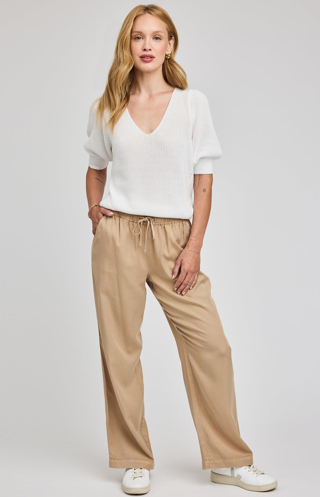 Woman wearing a white blouse and beige pants on a plain background