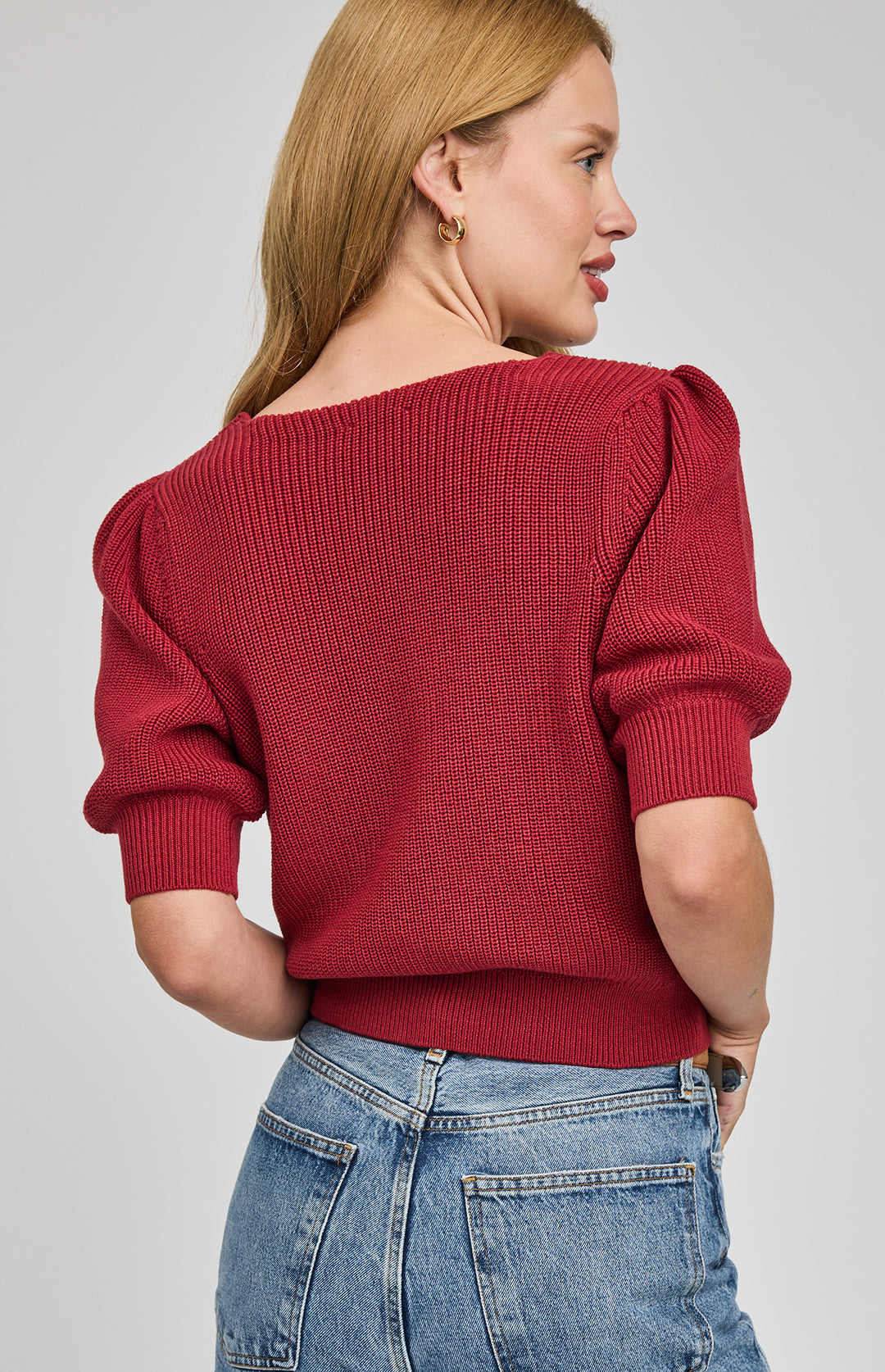 Woman wearing a red sweater with puffed sleeves on a gray background