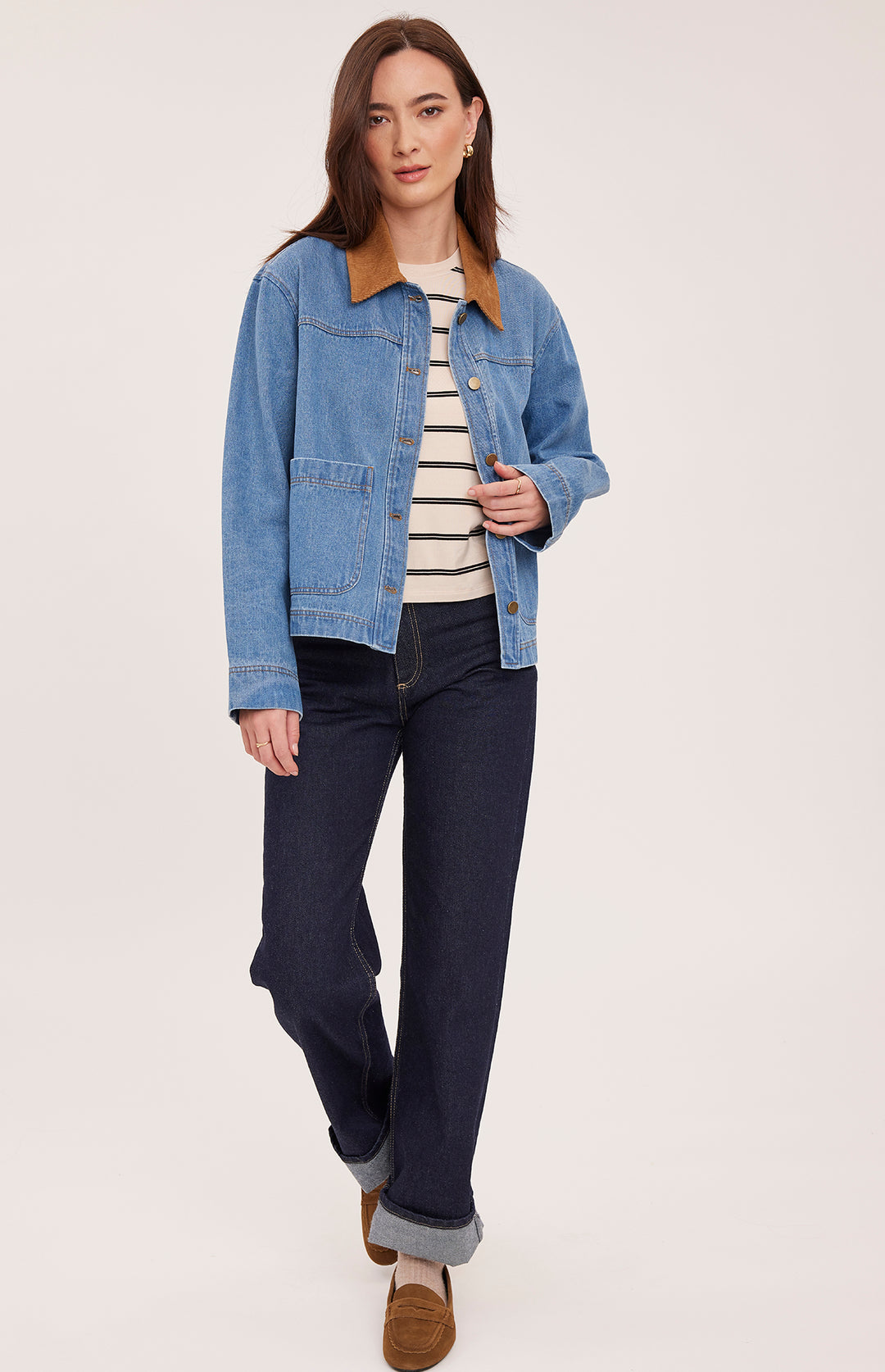 Woman wearing a blue denim jacket and navy jeans on a white background