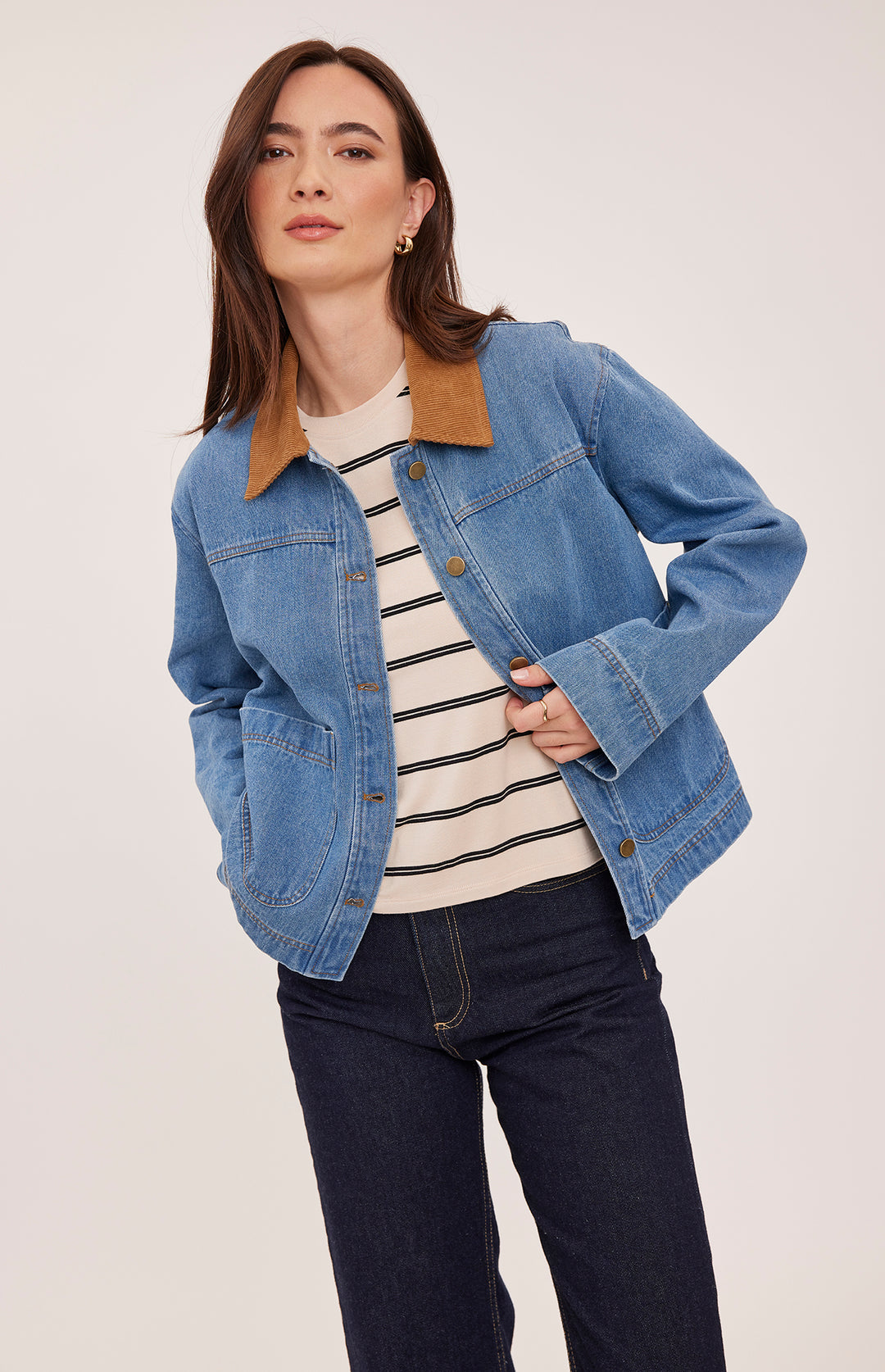 Woman wearing a blue denim jacket with a striped shirt and dark jeans on a white background