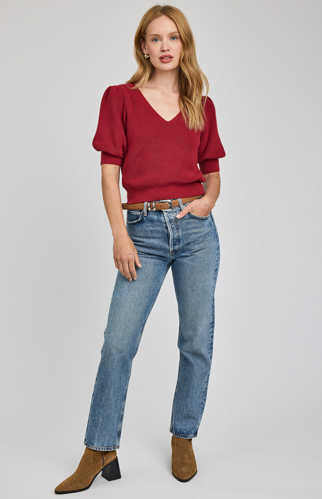 Woman wearing a red sweater and blue jeans on a gray background