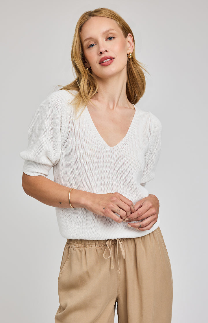 Woman wearing a white sweater and beige pants on a plain background