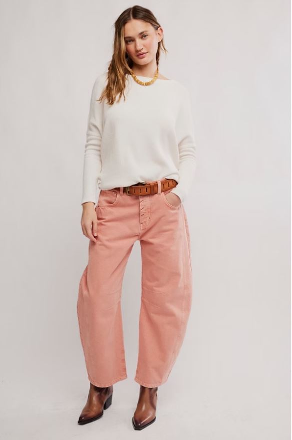 A woman modeling a white long-sleeve knit top and wide-leg dusty pink pants with a brown belt, styled with brown pointed-toe ankle boots against a light gray studio background.
