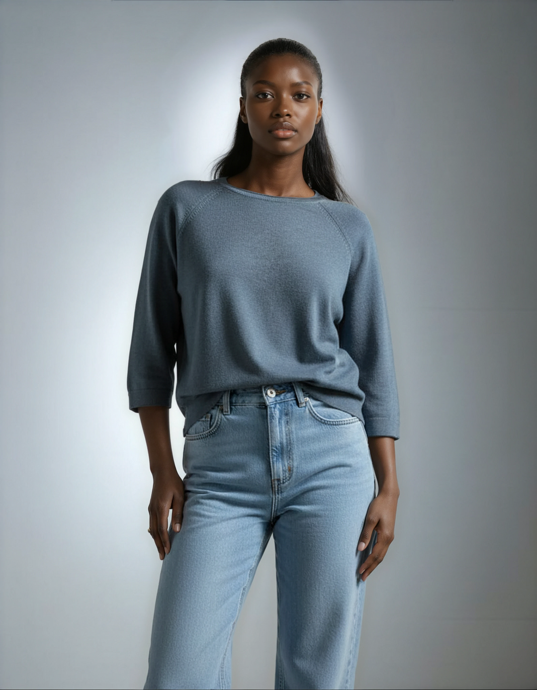 Woman wearing a blue sweater and light blue jeans against a gray background