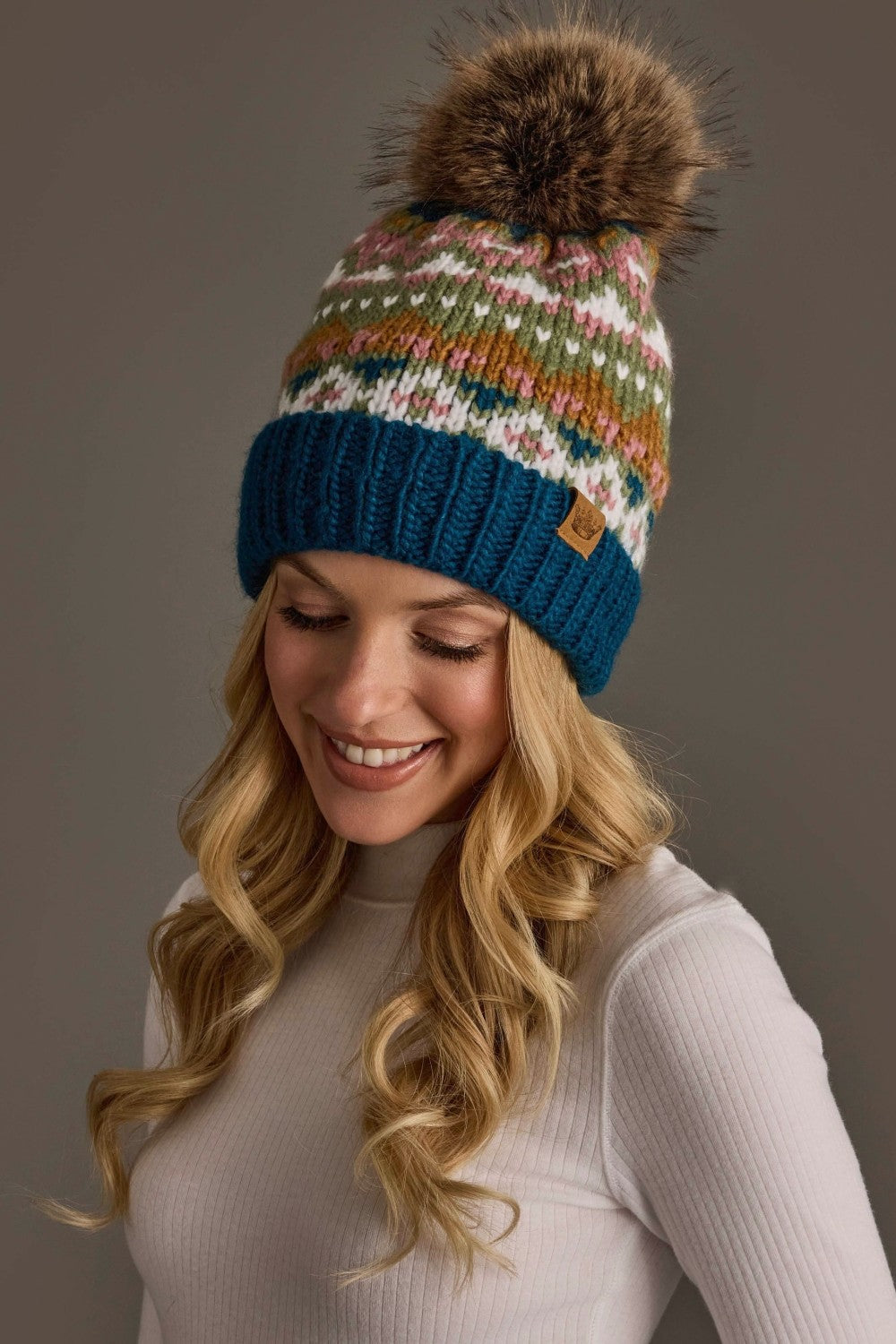 Woman wearing a colorful knit beanie with a pom-pom on a gray background